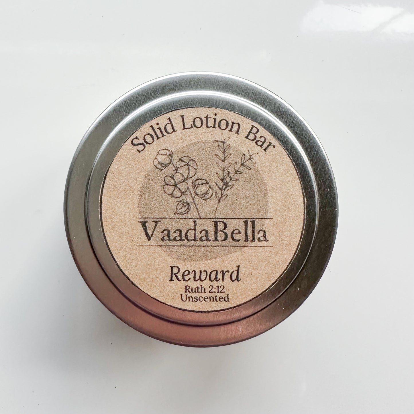 Bird's-eye view of a circular silver metal tin with brown kraft paper circle label centered. Logo, "Solid Lotion Bar" "reward" "Ruth 2:12" "Unscented" is all printed in black ink