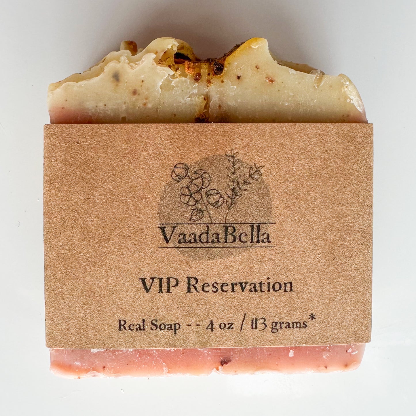 Pink bottom, light yellow topped bar with citrus zest sprinkled through out. Brown kraft paper product sleeve centered on the bar. Black ink printed logo, "VIP Reservation" and Real Soap -- 4 oz / 113 grams*