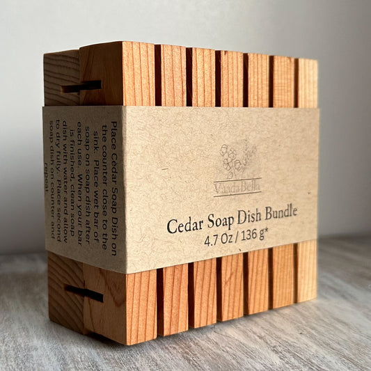 Two cedar planks with slots bundled together with brown kraft paper sleeve centered around the  planks.  Black ink print reads "Cedar Soap Dish Bundle, 4.7 oz / 136 g*"