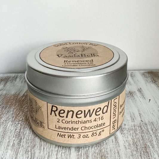 Front view of a circular silver metallic tin with lid.  brown kraft paper circle label centered. on the top, Logo, "Solid Lotion Bar" "Renewed" "2 Corinthians 4:16" "Lavender Chocolate" is all printed in black ink.  On the front, brown kraft paper sleeve wraps around the side of the tin with "Renewed" "2 corinthians 4:16" "Lavender Chocolate" "Net wt. 3 oz, 85 g*" printed on it