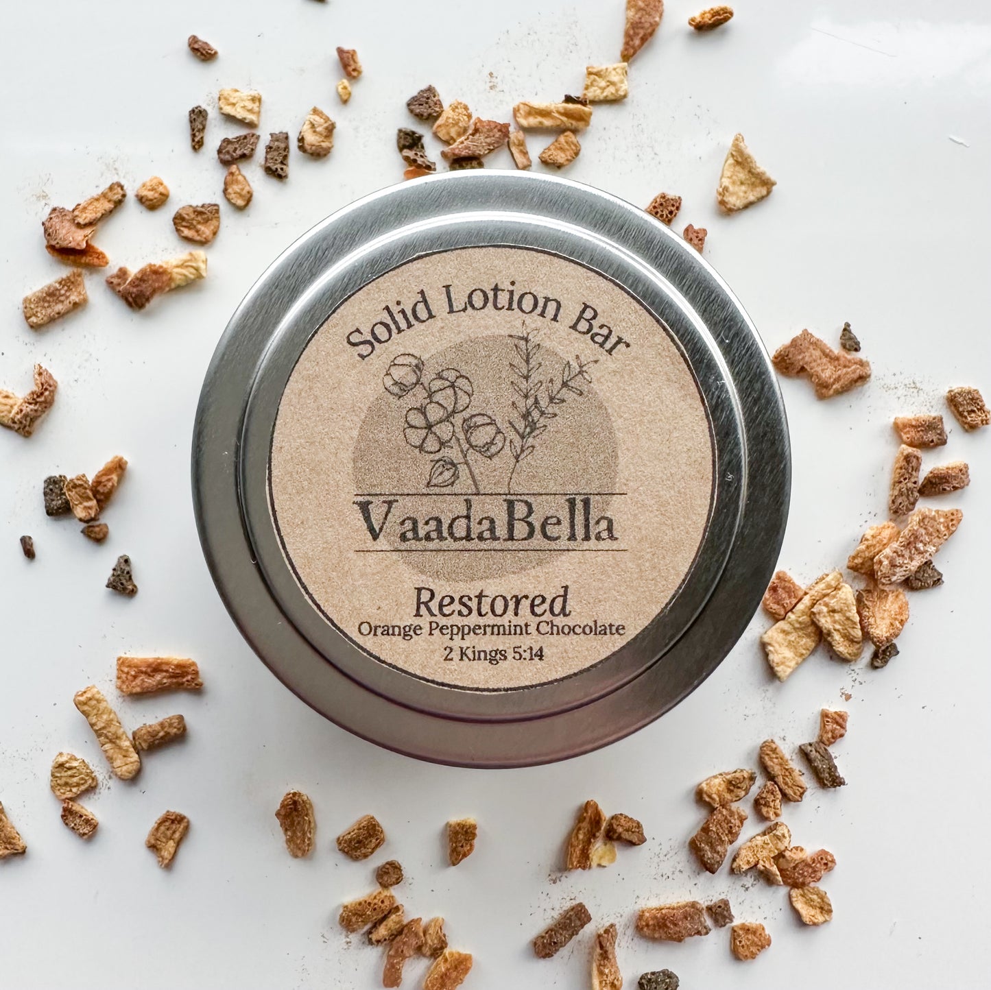 Bird's-eye view of circular silver metallic tin with circular kraft paper label centered on the top.  "Restored" "2 Kings 5:14" "Orange Peppermint Chocolate" is printed on the label in back ink.
