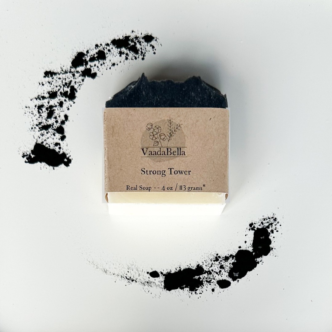 White bottom, black bar with kraft paper product sleve centered on bar.  Black ink prints the brand logo, "Strong Tower" and "Real Soap -- 4 oz / 113 grams*".  Activated charcoal powder at the upper left and lower right of the image.