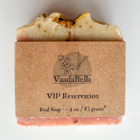 Pink bottom, light yellow topped bar with citrus zest sprinkled through out.  Brown kraft paper product sleeve centered on the bar.  Black ink printed logo, "VIP Reservation" and Real Soap -- 4 oz / 113 grams*