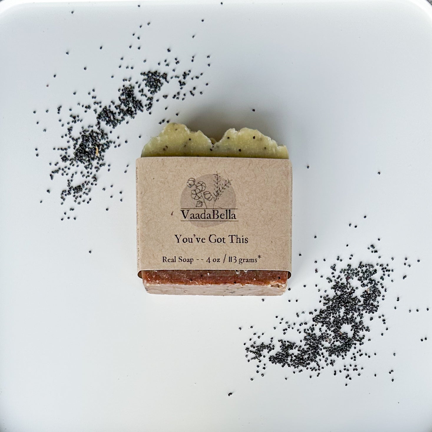 Brown bottom, light yellow top with dots bar with kraft paper product sleeve centered on bar.  Black ink prints the brand logo, "You've Got This" and "Real Soap -- 4 oz / 113 grams*".  Scattered poppy seeds in the top left and lower right.