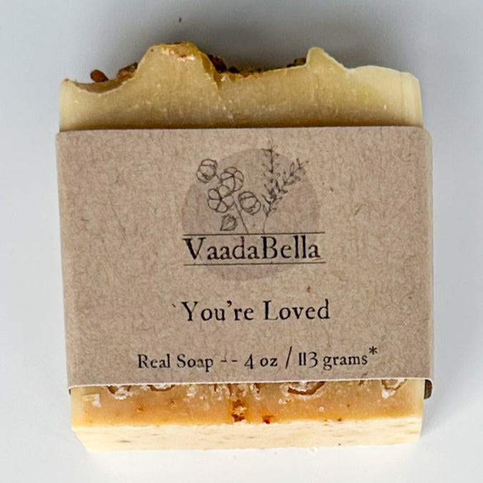 Yellow orange bottom with slightly lighter top with kraft paper product sleeve centered on bar.  Black ink prints the brand logo, "You're Loved" and "Real Soap -- 4 oz / 113 grams*"